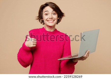 Young smiling cheerful happy smart IT woman wear pink sweater hold use work on laptop pc computer show thumb up isolated on plain pastel light beige background studio portrait People lifestyle concept Royalty-Free Stock Photo #2259128269