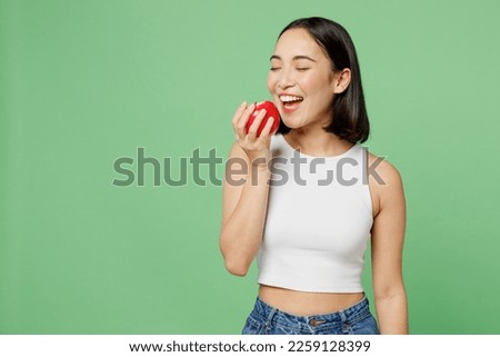 Young vegetarian woman wear white clothe s hold in hand biting ripe red apple close eyes isolated on plain pastel light green background. Proper nutrition healthy fast food unhealthy choice concept Royalty-Free Stock Photo #2259128399