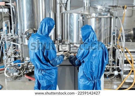 Back view of two workers using control panel while operating equipment at chemical factory
