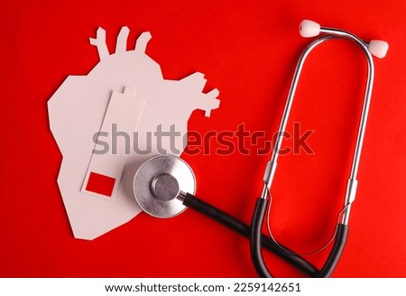 Paper cut anatomical heart and low battery, stethoscope on red background. Diagnosis Heart disease