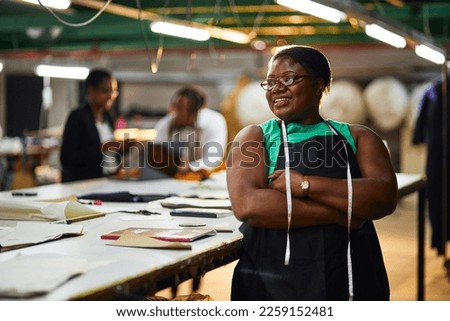 african female business woman textile industry wearing a green shirt with black apron measuring tape with arms folded Royalty-Free Stock Photo #2259152481