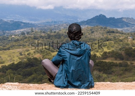Young man sitting. He is looking at the landscape at sunrise in Guavata, Santander. Royalty-Free Stock Photo #2259154409