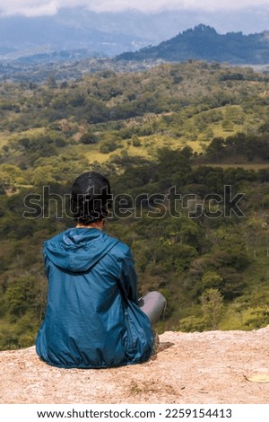Young man sitting. He is looking at the mountains at sunrise in Guavata, Santander. Royalty-Free Stock Photo #2259154413