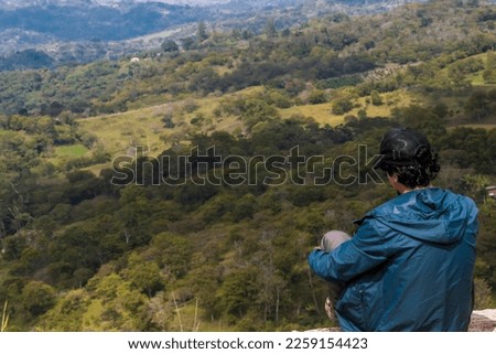 Young man sitting. He is looking at the landscape at sunrise in Guavata, Santander. Royalty-Free Stock Photo #2259154423