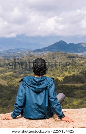 Young man relaxing. He is looking at the landscape at sunrise in Guavata, Santander. Royalty-Free Stock Photo #2259154425