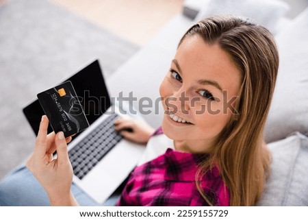 Over shoulder view of pretty woman shopping online on laptop and holding credit card while looking and smiling at camera