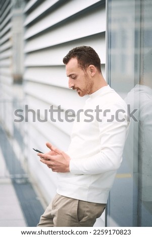 Vertical view of the serious businessman checking email, watching videos near building wall. Young stylish man chatting, reading text message on the street. Shopping online concept