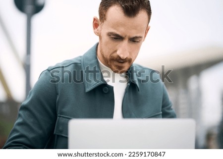 Young attractive business man working laptop online while sitting at outdoors workplace alone. Technologies and people concept