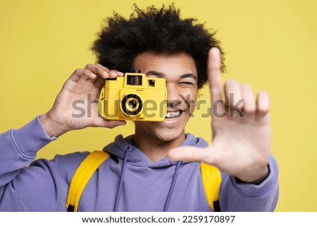 Young smiling African American photographer taking pictures isolated on yellow background. Close up portrait of happy attractive tourist holding photo camera. Vacation, travel concept 