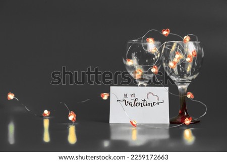 Dining concept - two wine glasses filled with light bulbs chain with romantic note be my Valentine isolated on grey - valentine concept with copy space for background, offers, post, posters, banners.
