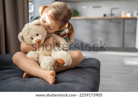 Cute little girl hugging teddy bear while sitting on sofa at home. High quality photo Royalty-Free Stock Photo #2259173905