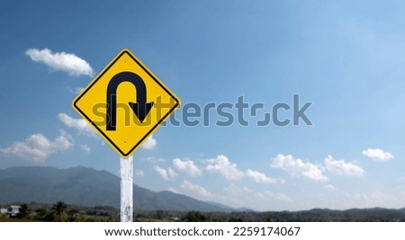 Traffic sign: Right U-turn sign on cement pole beside the rural road with white cloudy bluesky and mountains background, copy space.