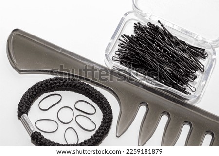 Black comb with a box full of hairpins and hair bands of different sizes on a white background.