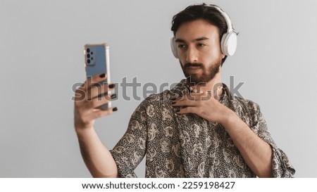 Panoramic photo of a young gay man staring at his cell phone while using headphones.