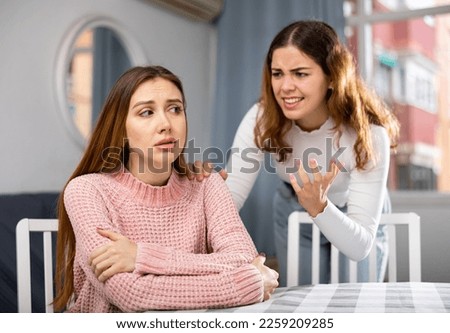 Unhappy woman sitting at table while her angry relative or wife gesturing hands and blaming her, family conflict