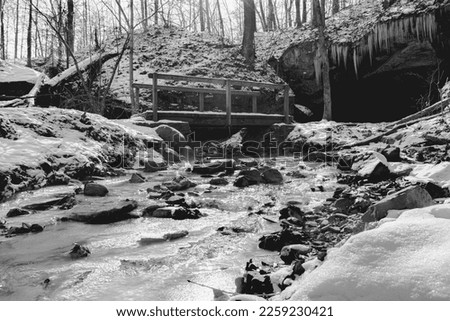 Black and white bridge over icy stream with cave