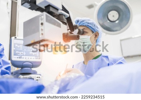 Male doctor doing surgery inside modern operating theater in surgical hospital.Microscope was use in eye surgery.Surgeon in blue sterile suit working with microscope with light effect.Medical concept. Royalty-Free Stock Photo #2259234515