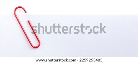 Red paper clip attached to multiple sheets of white paper in wide format.