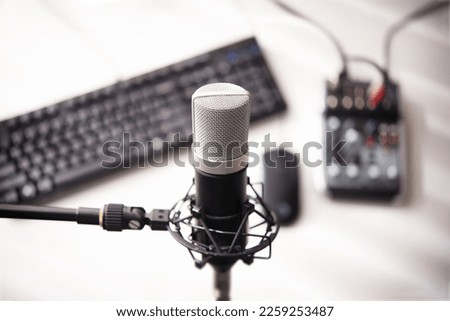 Broadcast, live stream, talk, voice recording, webinar, concept.  A large condenser microphone in a mic holder on a stand. with PC, mouse and mixer on table. shallow depth of field.