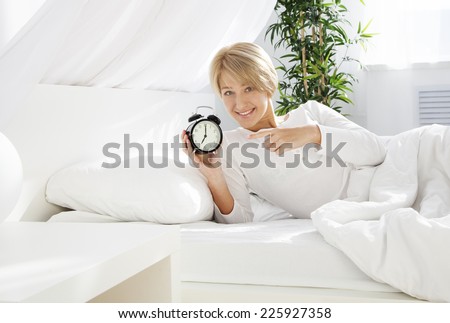 beautiful woman in the morning in bed, showing on the clock