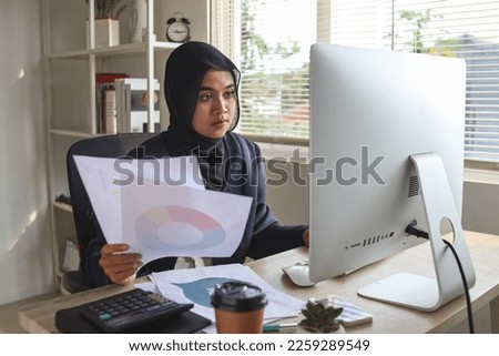 Asian muslim business woman behind paper work, tired and frustrated. Working in office, looking at documents and financial reports. Royalty-Free Stock Photo #2259289549