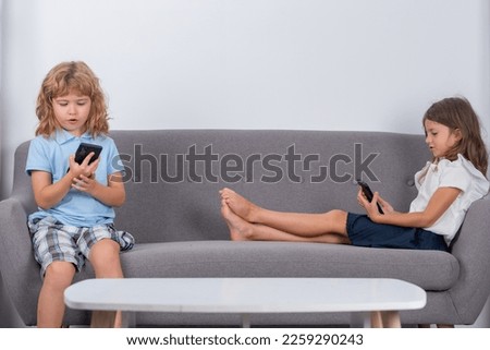 Two kids alone with phone at home. Little cute kids playing smartphone. Brother and sister at home playing video games. Child addicted phone. Kids playing smartphone watching cell phone.