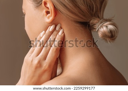 Inflamed tonsillar lymph nodes. Young woman touches enlarged lymph nodes under jaw on her neck with hand on dark background. Flu, cold, tonsillitis, sars virus, inflamed tonsils, bacterial infection Royalty-Free Stock Photo #2259299177