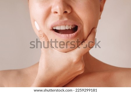 Cropped shot of a young woman suffering from jaw pain holding her chin isolated on a beige background. Inflammation of cervical lymph nodes, Diseases of ENT organs, facial, trigeminal nerve, toothache Royalty-Free Stock Photo #2259299181