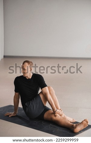 An athletically built man does yoga in the gym on a mat.