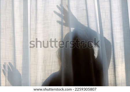 Silhouette of a woman behind a semi transparent curtain.  Depression, sadness and loneliness concept. 