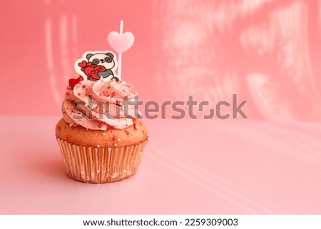 Strawberry Cupcake topped with a chocolate panda holding the wording " Love" on Pastel Pink Background