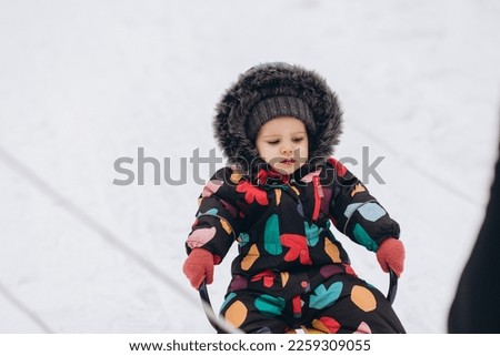 Little girl sledging downhill an having fun. Pink sledge and jacket, colorful scarf