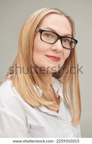 Shot of a happy beautiful middle aged businesswoman in a classic white blouse and spectacles. Grey studio background. Glasses style. 