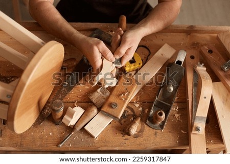 Closeup shot of unrecognizable faceless man carpenter making a handmade wooden toy in a home workshop, working on table among carpentry tools, wood carving. Royalty-Free Stock Photo #2259317847