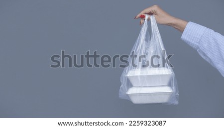 Woman's hands holding PVC plastic bag with takeaway foam lunch boxes. Single use food containers, donation concept. Royalty-Free Stock Photo #2259323087