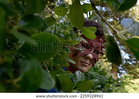 portrait of handsome brunette man wearing fantasy medieval prince costume with greenmail leather mask and romantic silk shirt, posing in a forest location with tree foliage background. 