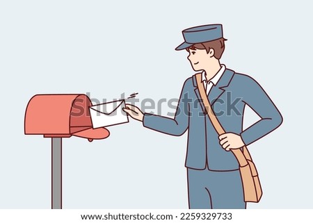 Man in postman uniform throws paper letter into metal mailbox located on street. Guy delivers fresh mail with alerts from government agencies or messages from friends Royalty-Free Stock Photo #2259329733