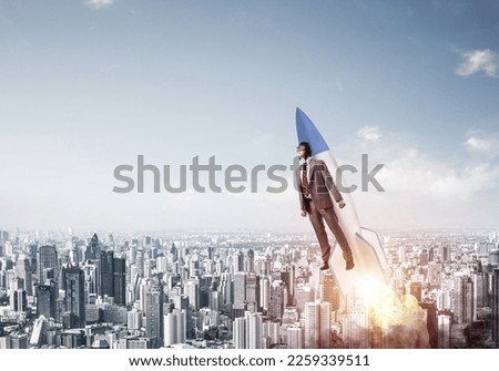 Business person in aviator hat flying on rocket. Progress and innovation technology. Corporate businessman flying with jetpack rocket in blue sky above modern city. Leadership motivation concept. Royalty-Free Stock Photo #2259339511