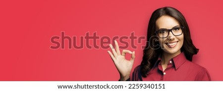 Face portrait image - smiling brunette business woman in eye wear glasses, spectacles, isolate on red colour background. Businesswoman, bank manager, real estate sales agent showing okay ok gesture