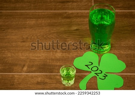 Shamrock shot glasses lined up against black background filled with emerald green spirit cocktail to be drunk at celebrations for St Patrick's day. Irish holiday is drinking event when people party