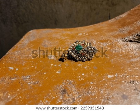 Stock photo of beautiful golden color saree pin or brooch decorated with pearl, red, white stone, green color stone in the middle of the pin. Picture captured under bright sunlight. saree dripping pin