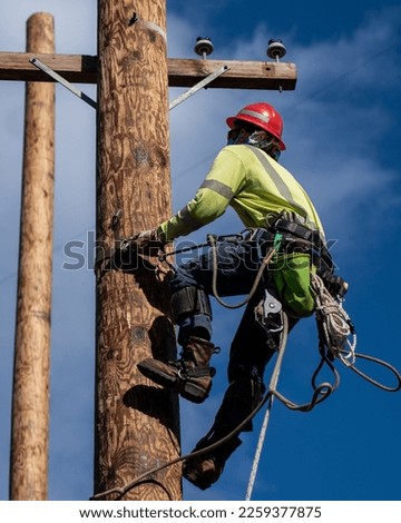 Lineman ascending utility pole with pole climbers Royalty-Free Stock Photo #2259377875