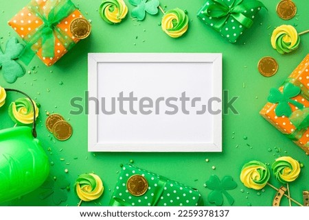 Saint Patrick's Day concept. Top view photo of empty photo frame present boxes pot meringue candies sprinkles gold coins and trefoils on isolated green background with copyspace