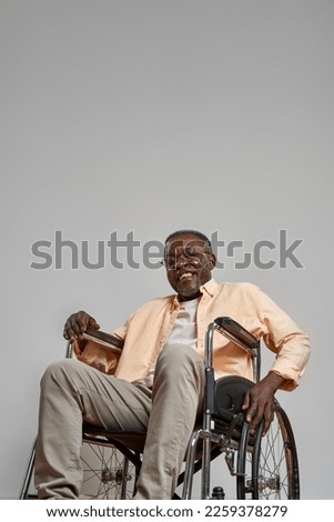 Smiling senior black man with disability on wheelchair looking at camera. Conquering adversity and willpower. Concept of modern elderly lifestyle. Isolated on grey background. Studio shoot. Copy space Royalty-Free Stock Photo #2259378279