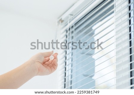 Female hand closing window jalousie. Open or close the window blinds in the room Royalty-Free Stock Photo #2259381749