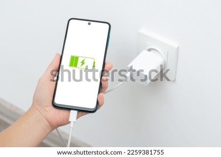 Female holding phone while charging from wall outlet. Charging phone with regular charger concept Royalty-Free Stock Photo #2259381755
