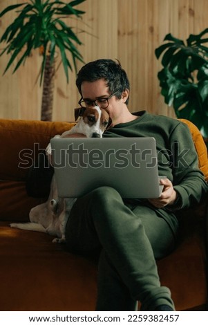 thirty-year-old man with laptop and dog sitting at home on the couch Royalty-Free Stock Photo #2259382457