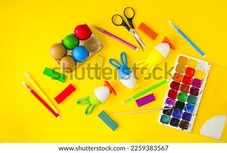 Easter layout on a yellow background, children's crafts, coloring Easter eggs.  On the table are multi-colored paints, plasticine.  Concept creative, holiday bright easter.  Flat lay.