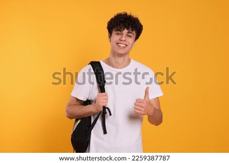 Handsome young man with backpack showing thumb up on orange background Royalty-Free Stock Photo #2259387787