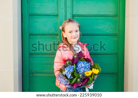 Portrait of adorable little girl on a street in a city, holding beautiful bouquet of autumn flowers